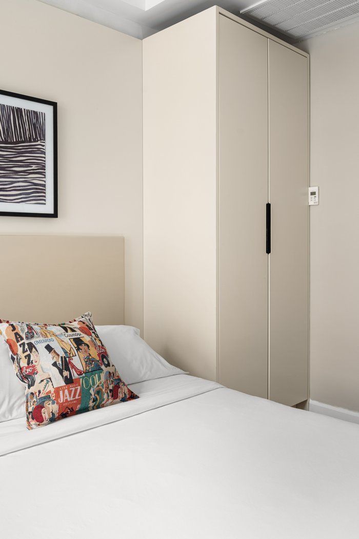 Bedroom with bed, tall cream closet, art print, and colorful pillow.