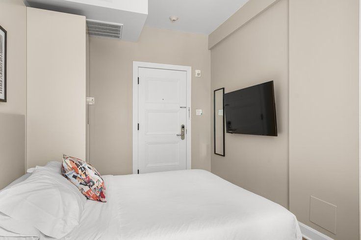 Small bedroom with white bedding, TV, and closed white door.