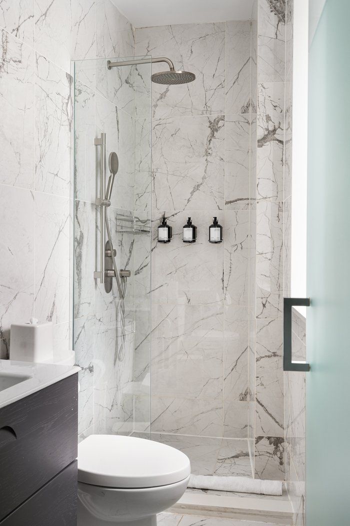 Shower with marble tile walls, glass door, toilet, and mounted soap dispensers.
