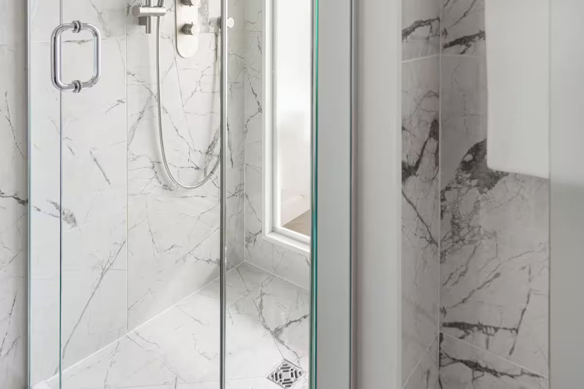 Shower with marble-patterned tile, glass door, and silver shower fixtures.
