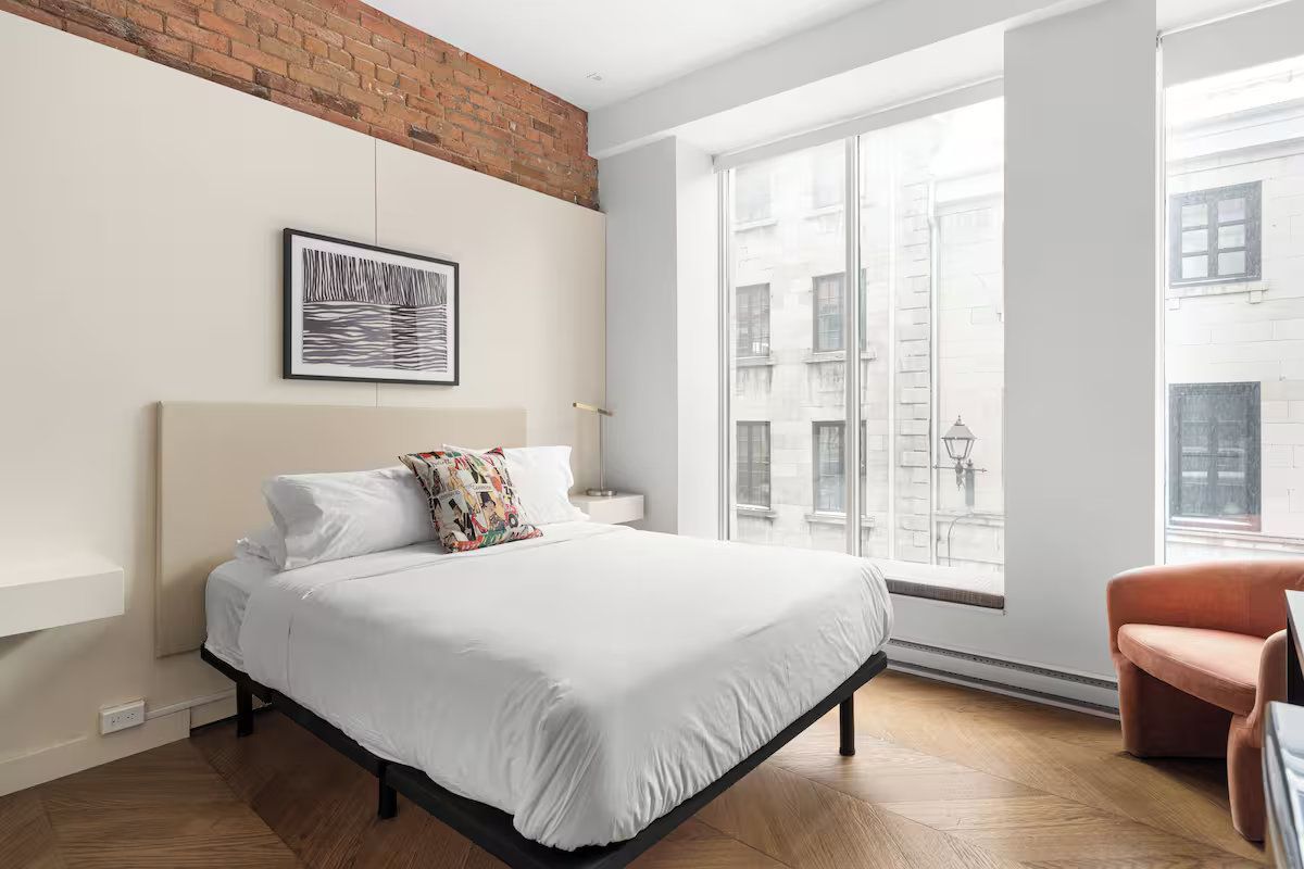Bedroom with a bed, large windows, and a brick accent wall; light and airy.