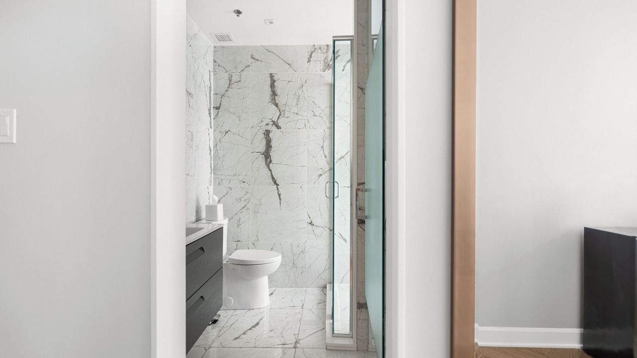 Bathroom with marble tile walls and floor, shower with glass door, black vanity, and white toilet.