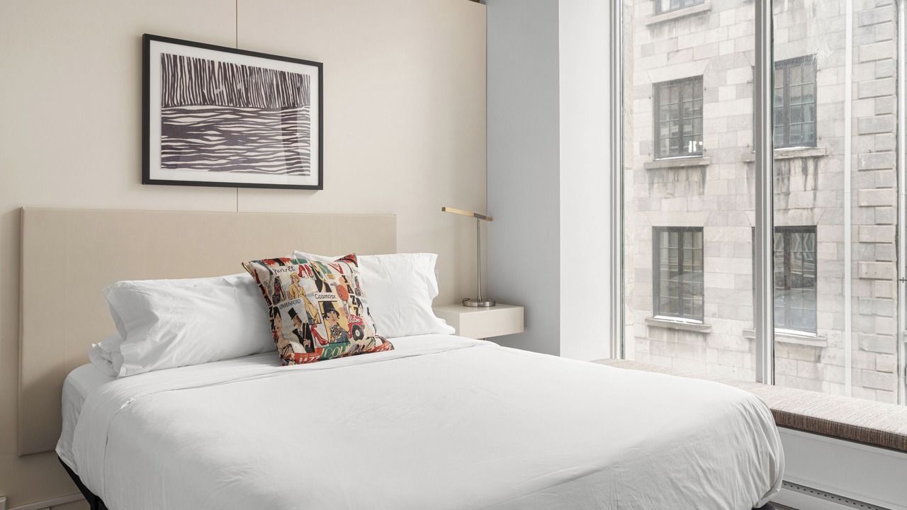 Bedroom with a bed, a window with a city view, and a framed artwork.