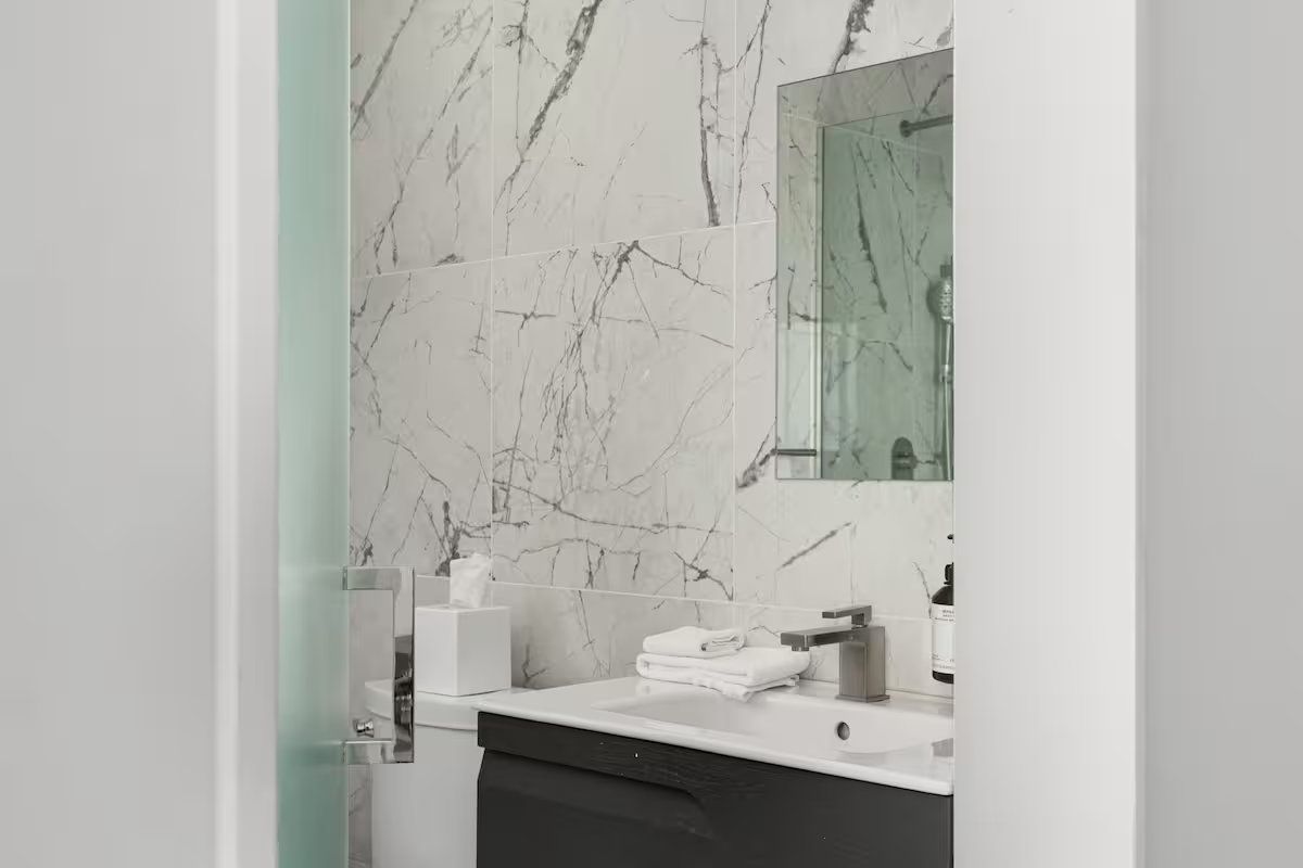 Bathroom interior with marble-like wall, vanity, and mirror, viewed from doorway.