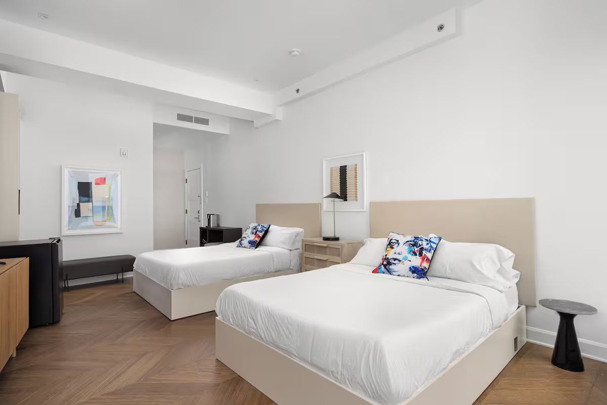 Bedroom with two beds, white walls, wood floors, and abstract art.