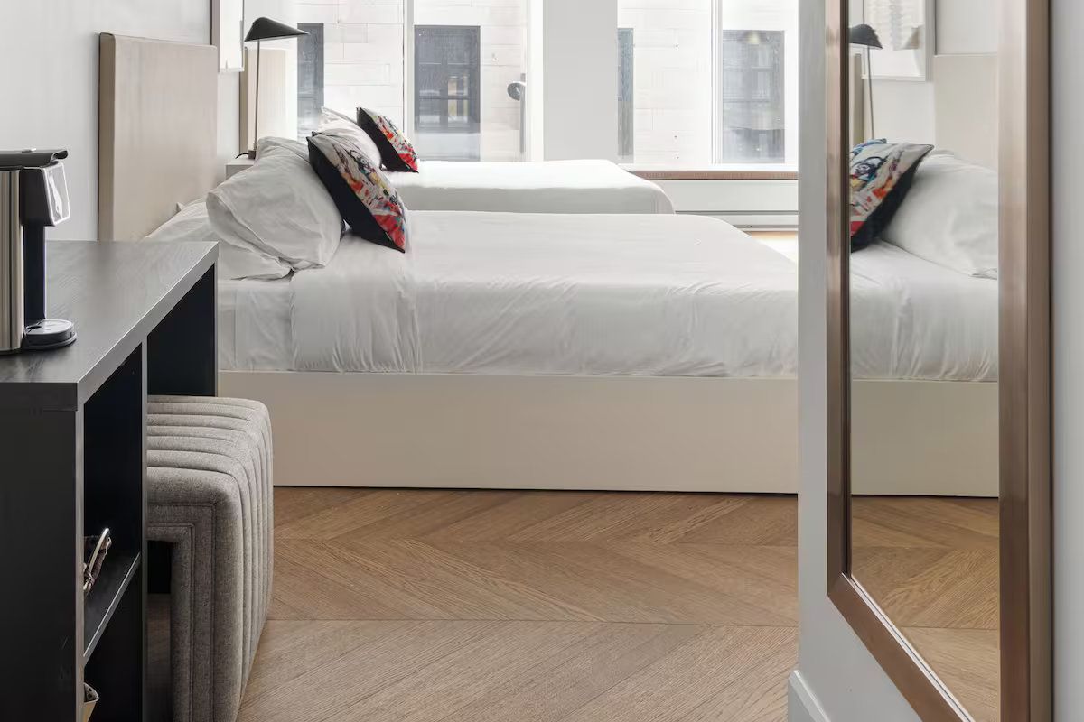 Two beds in a bright room with white linens, red pillows, and wooden floors.