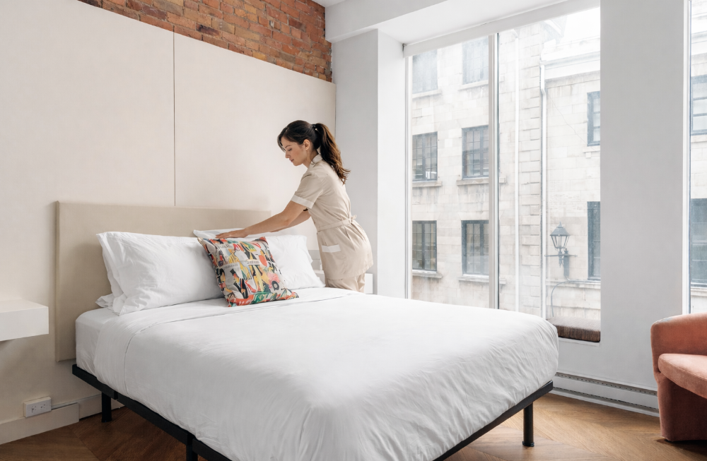 A man in a uniform pushes a service cart down a hotel hallway.