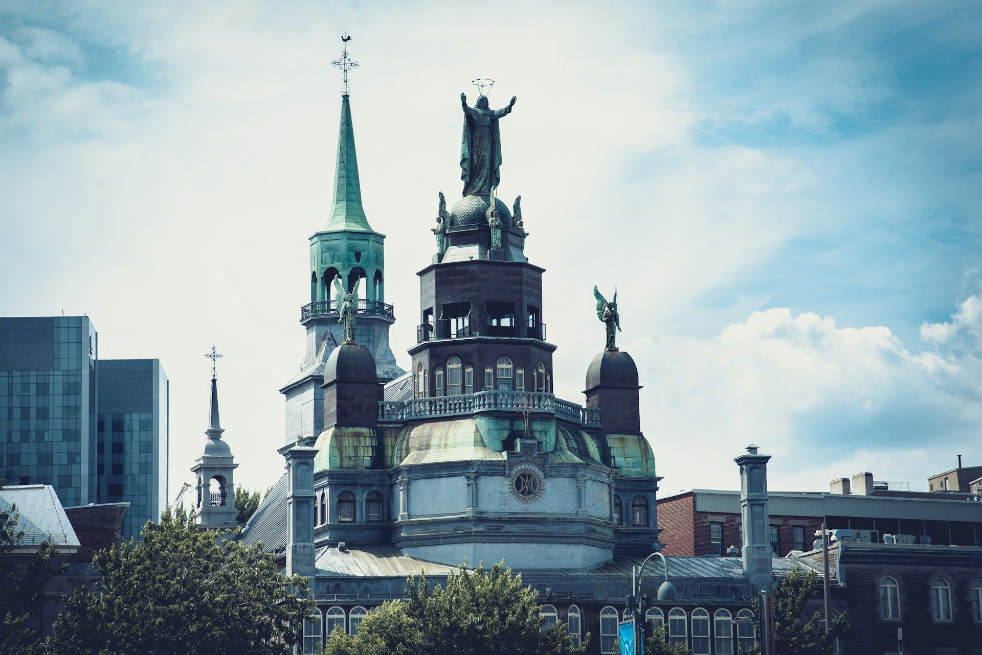 Ornate church with green spire and statue on the roof against a cloudy sky.