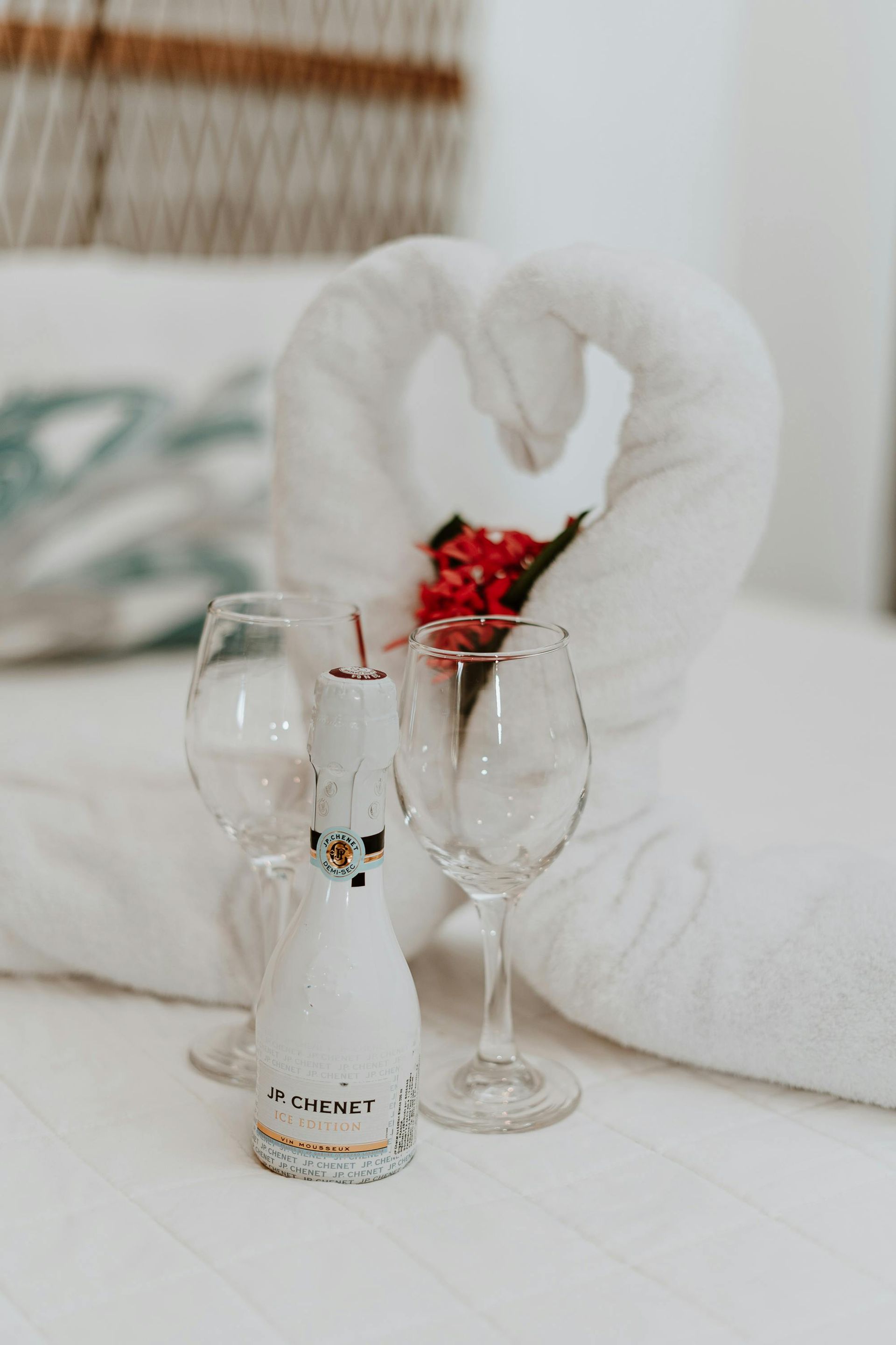 Champagne bottle and glasses on a bed with a towel swan decoration and flowers.