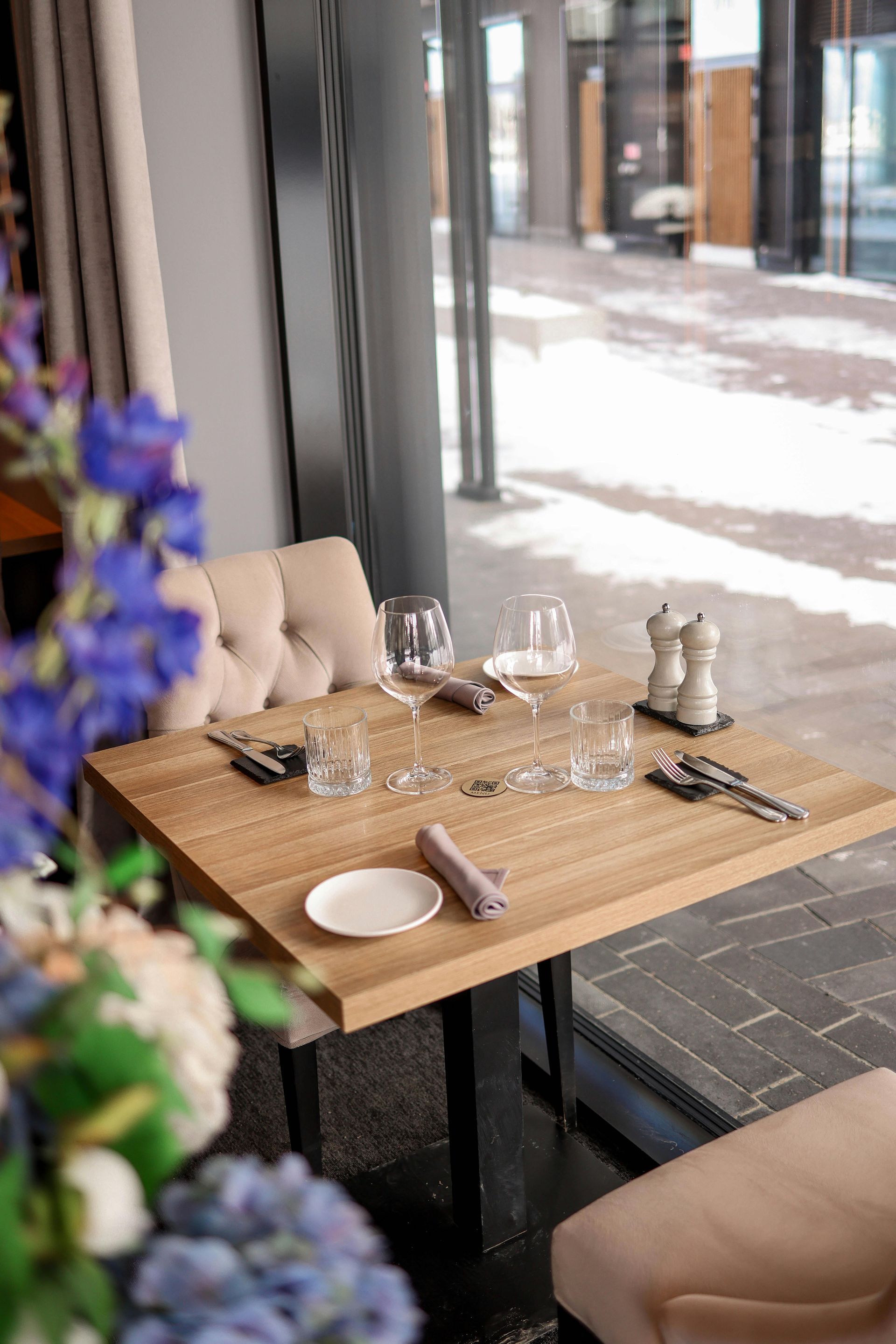 Restaurant table set for dining, with glasses, silverware, and plate. Window view of outdoors visible.