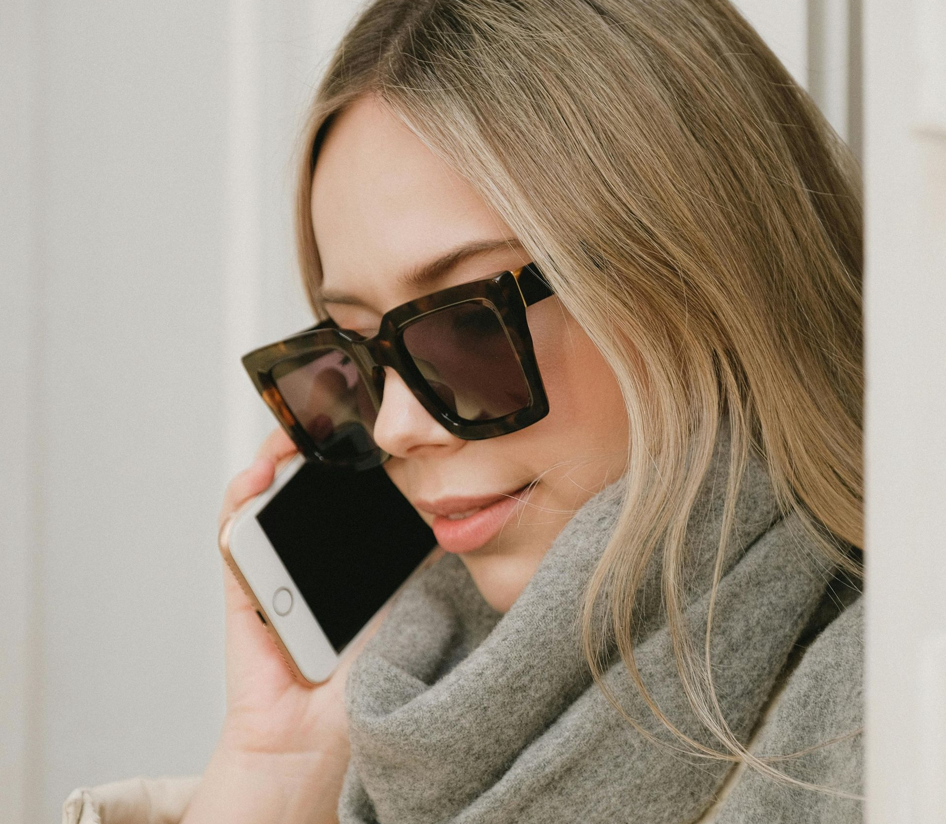 Woman wearing large sunglasses and a scarf talking on a cell phone.