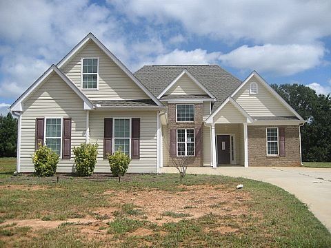 Tan two-story house with brick accents, blue sky, and a concrete driveway.