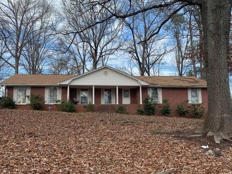 Red brick ranch house with brown roof and porch, on a hill covered in fallen leaves, under a blue sky.
