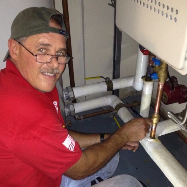 Worker in red shirt using a wrench on exposed plumbing inside a utility room