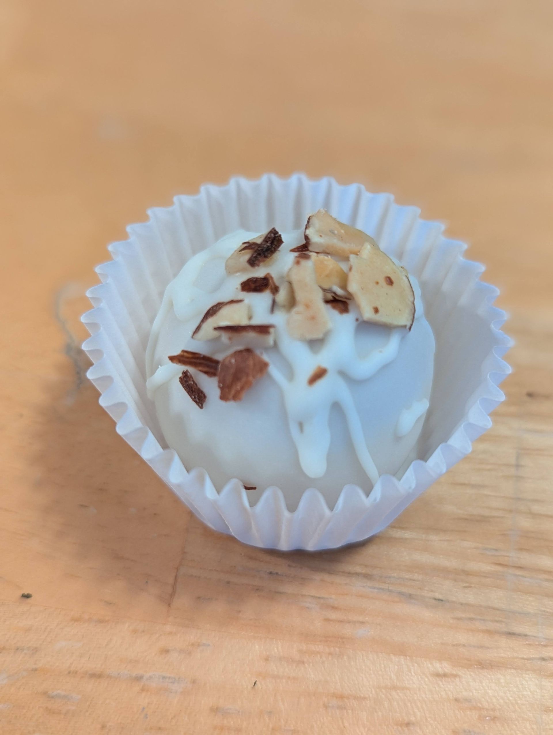 A white chocolate truffle with nuts on top in a paper wrapper