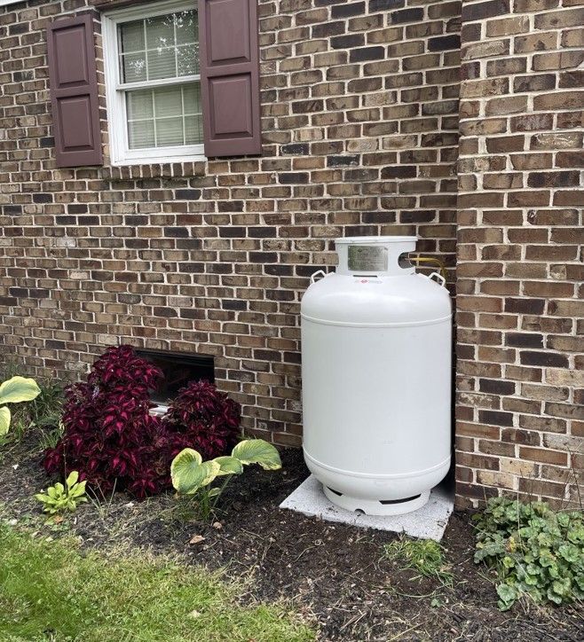 A white propane tank is sitting in a gravel area
