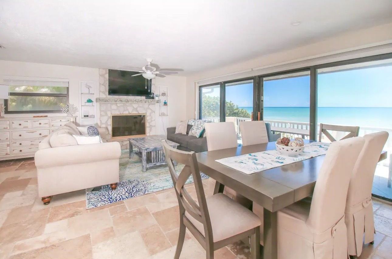 A living room with a dining table and chairs and a view of the ocean.