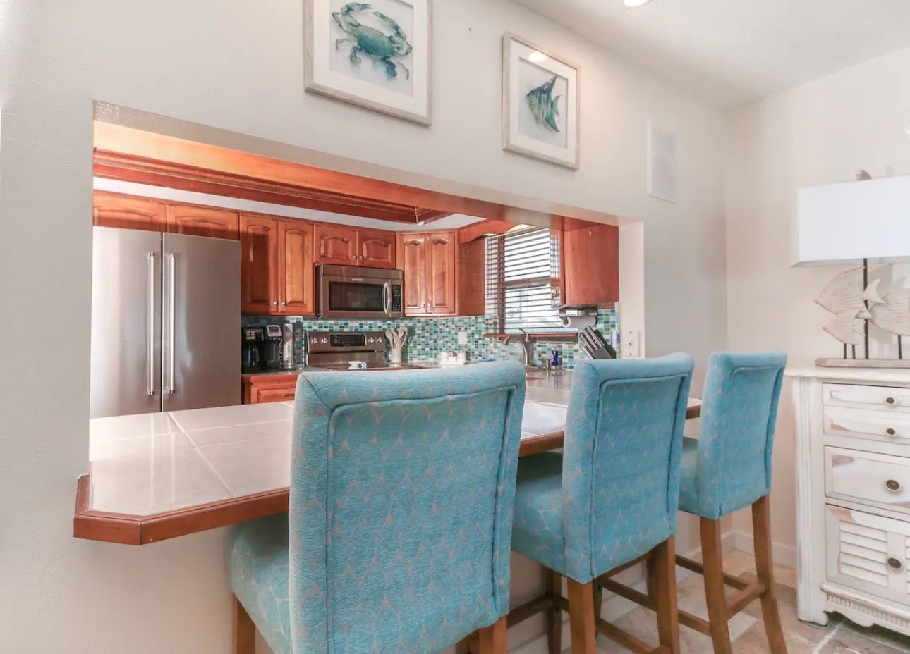 A kitchen with a bar and three blue chairs.
