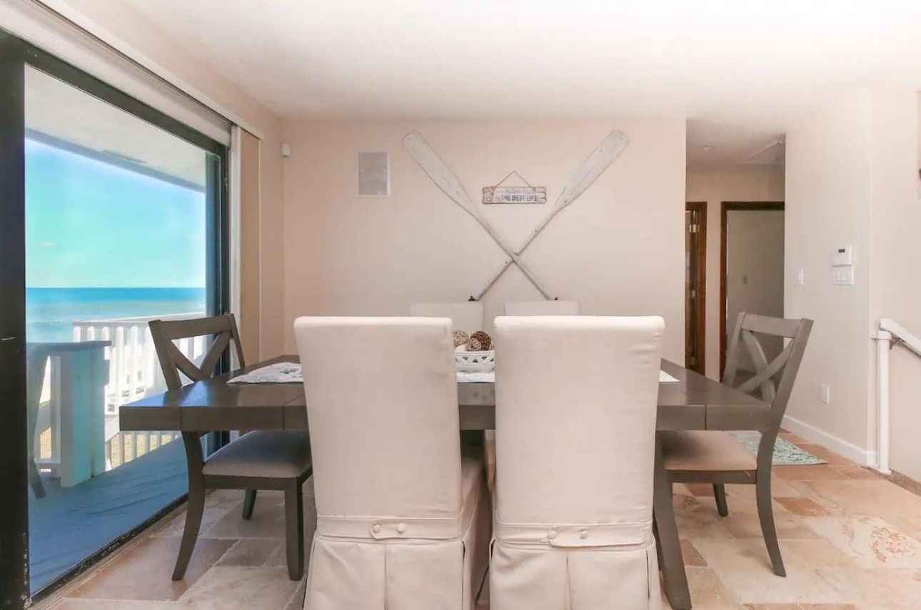 A dining room with a table and chairs and a view of the ocean.