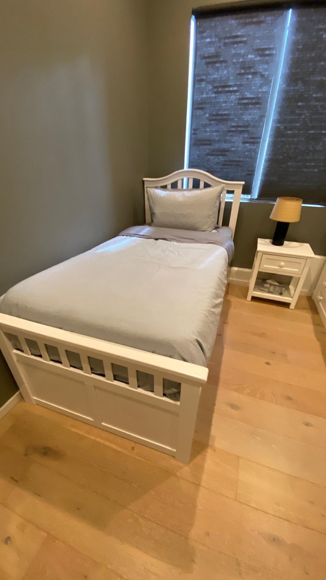 A bedroom with a single bed , nightstand , lamp and window.