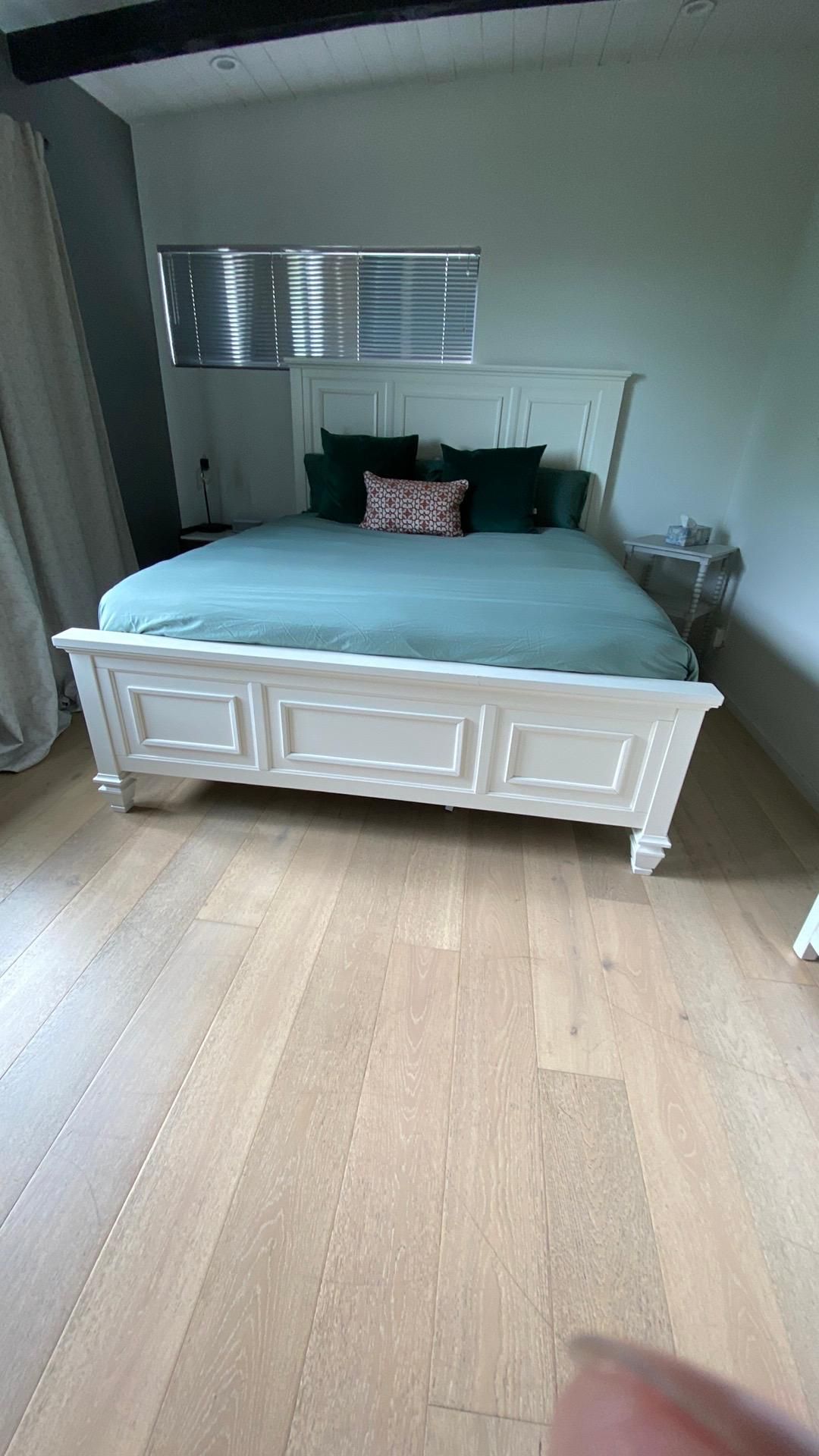 A white bed is sitting on a wooden floor in a bedroom.