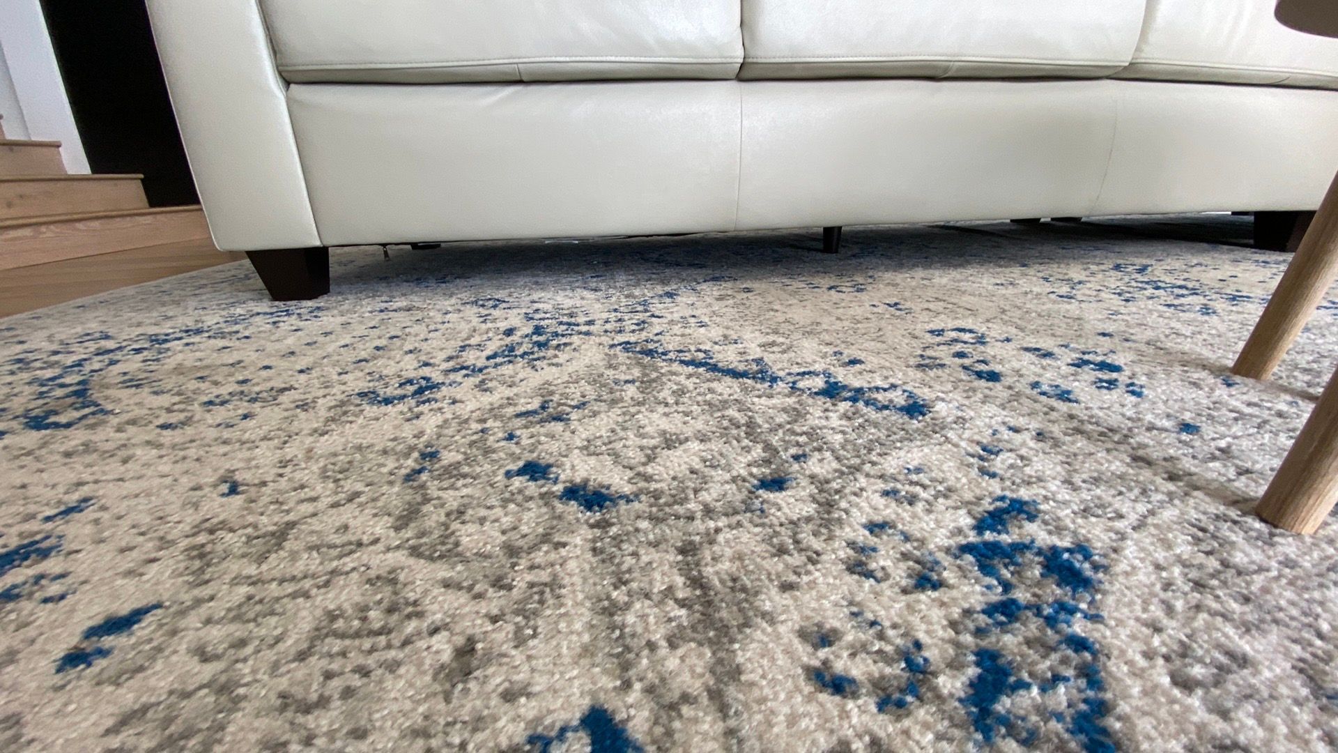 A white couch is sitting next to a blue rug in a living room.