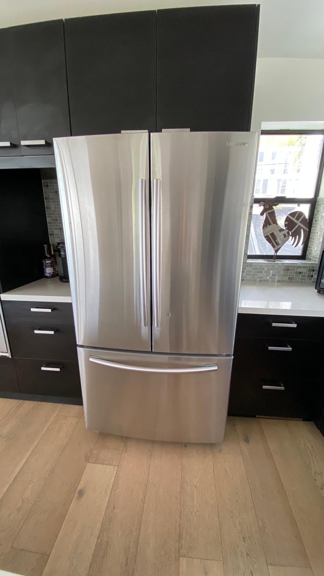 A stainless steel refrigerator is sitting in a kitchen next to a window.