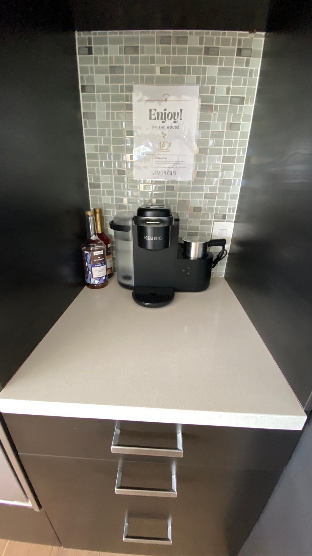 A kitchen counter with a coffee maker and a sign that says enjoy.