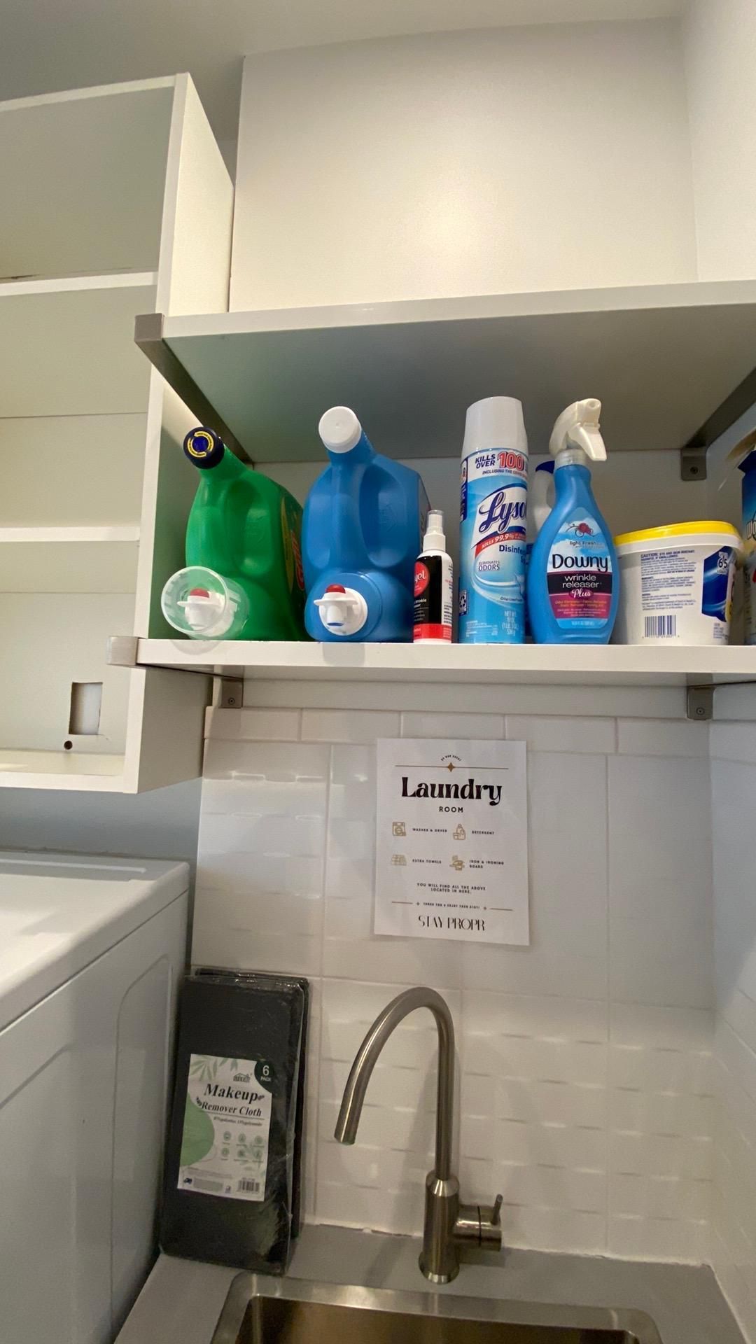 A laundry room with a sink , washing machine , and shelves filled with cleaning supplies.