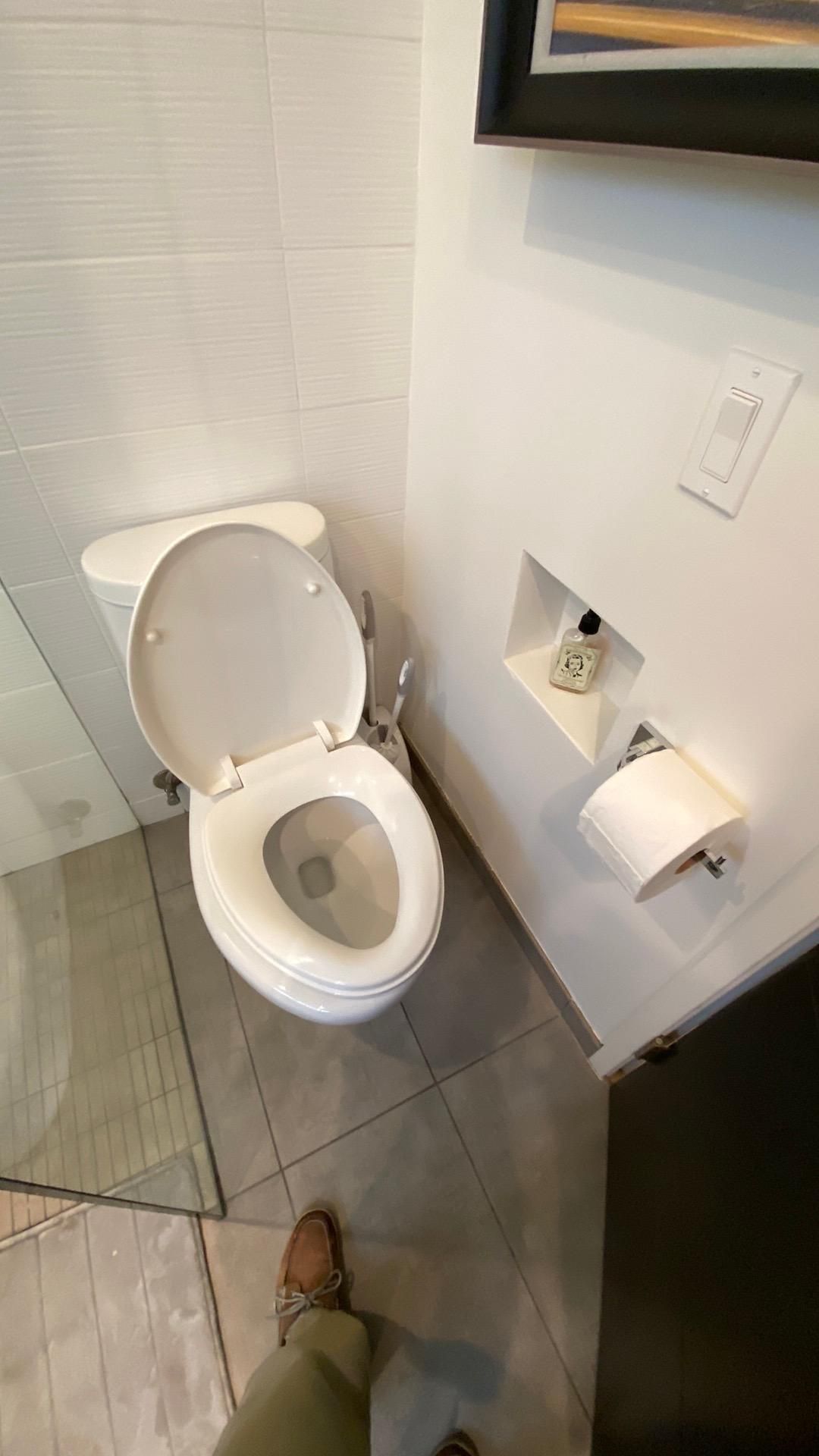 A person is standing next to a toilet in a bathroom.