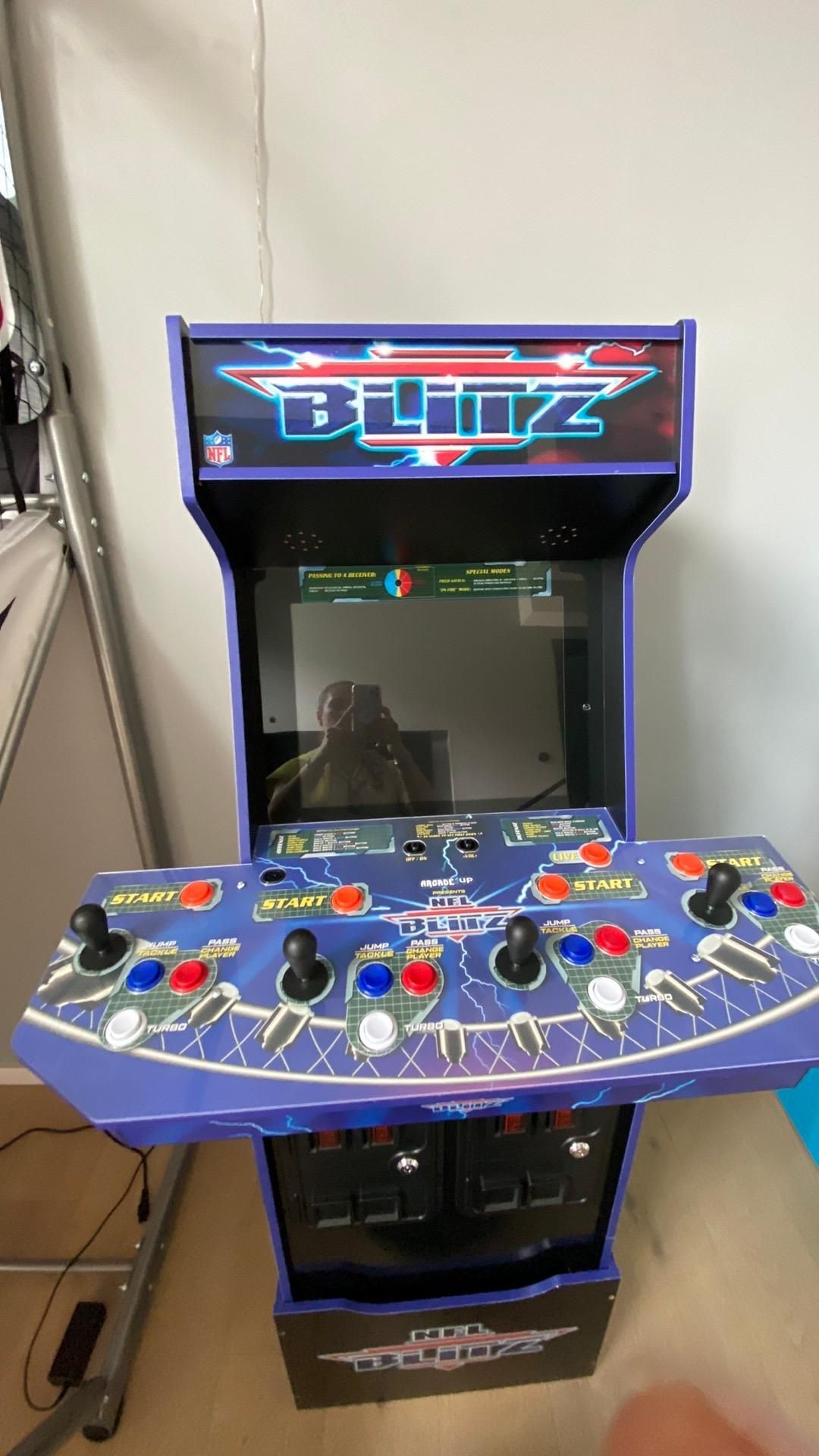 A blue arcade machine is sitting on a wooden floor in a room.