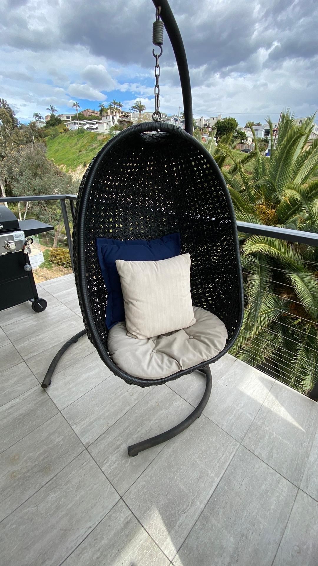 A hanging chair with a pillow on a balcony.