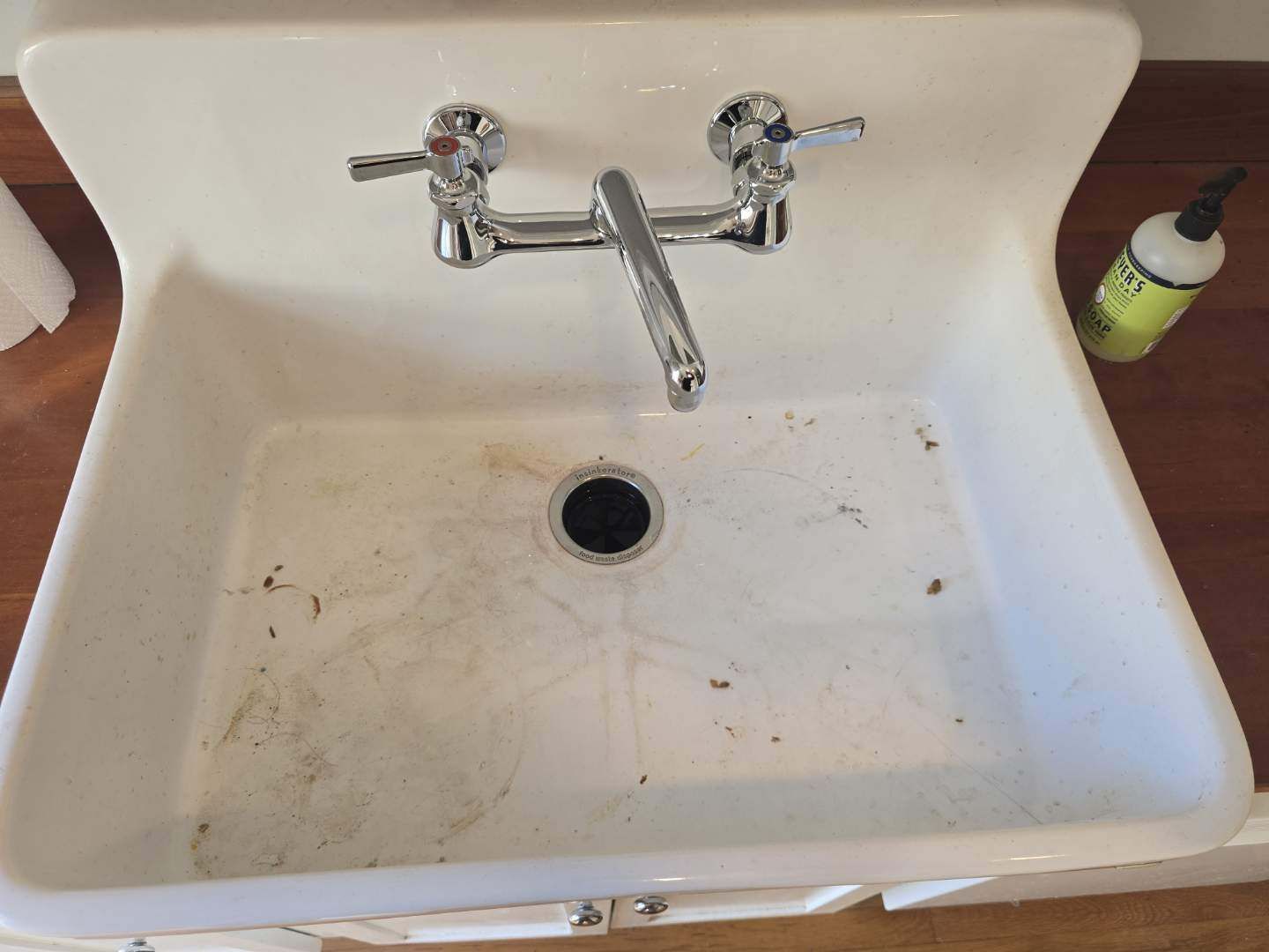 A dirty kitchen sink with a bottle of soap next to it