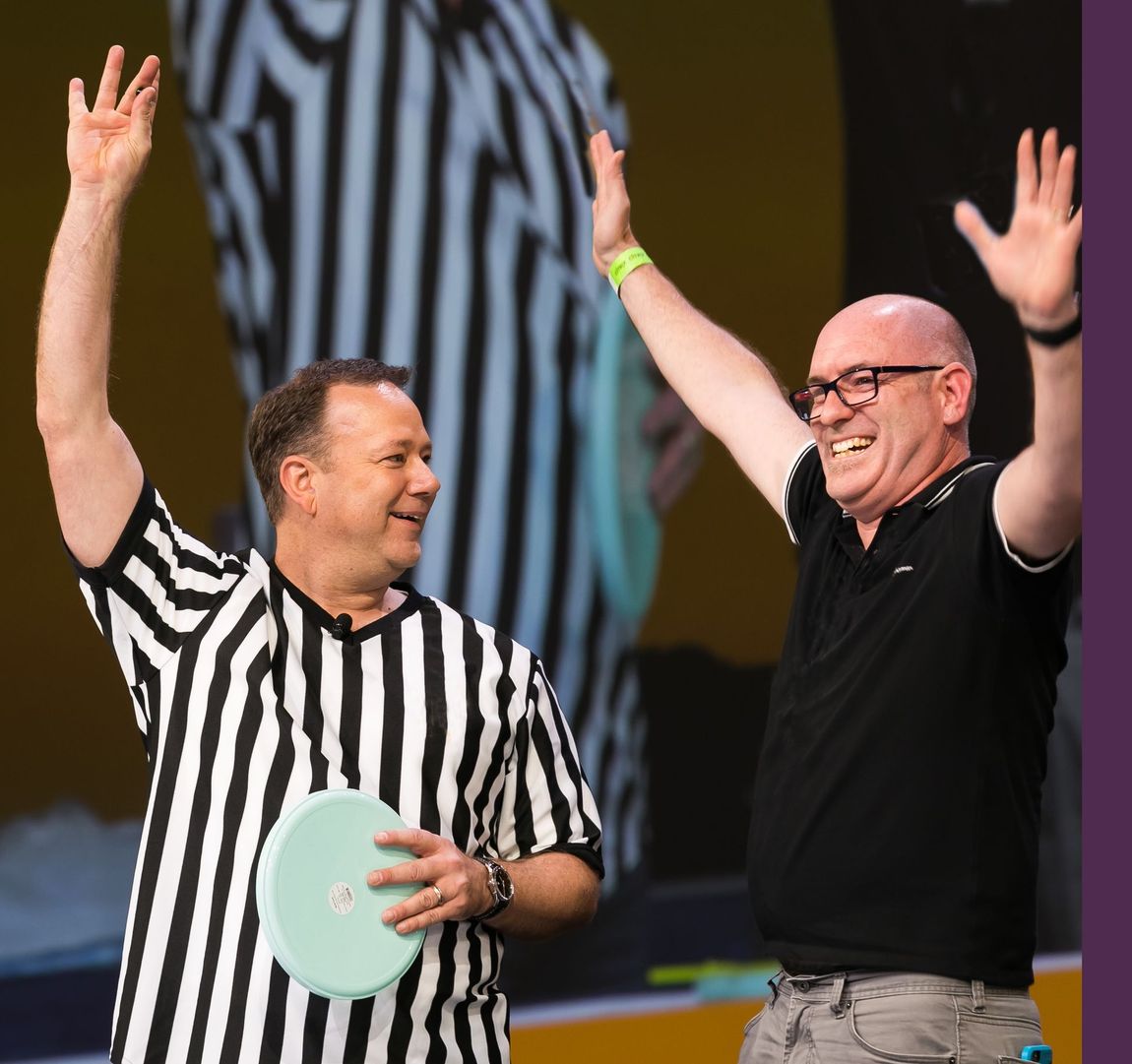 Two men in striped shirts are standing next to each other smiling with their arms in the air 