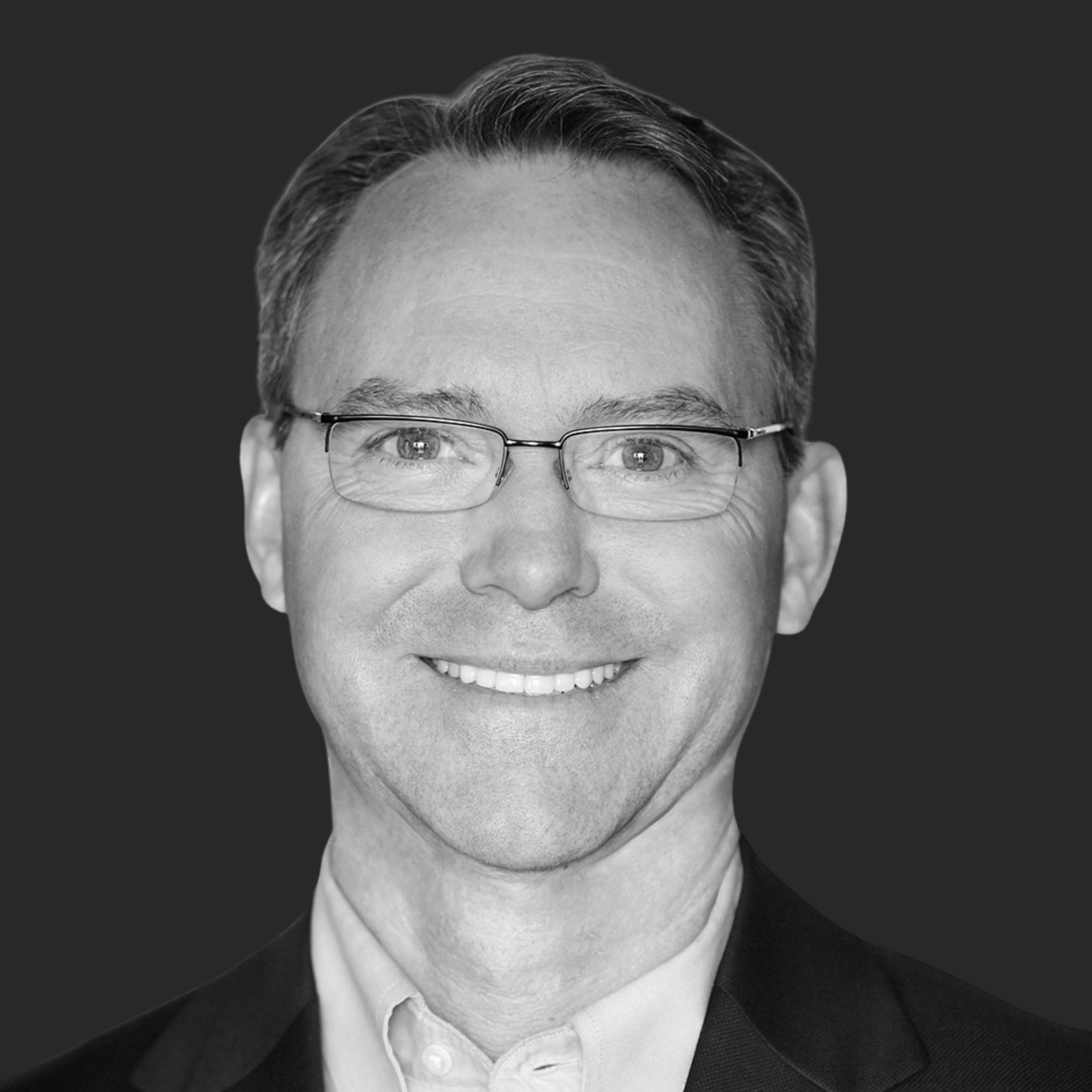 A man wearing glasses and a suit is smiling in a black and white photo.