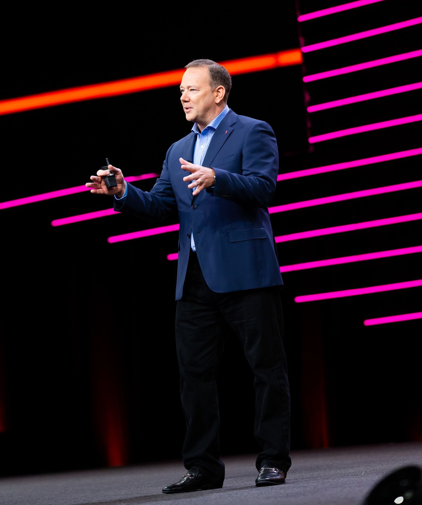 A man in a blue jacket is standing on a stage giving a speech.