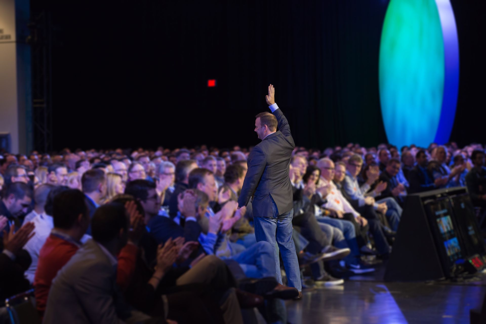 A man is standing on a stage raising his hand in front of a crowd of people.