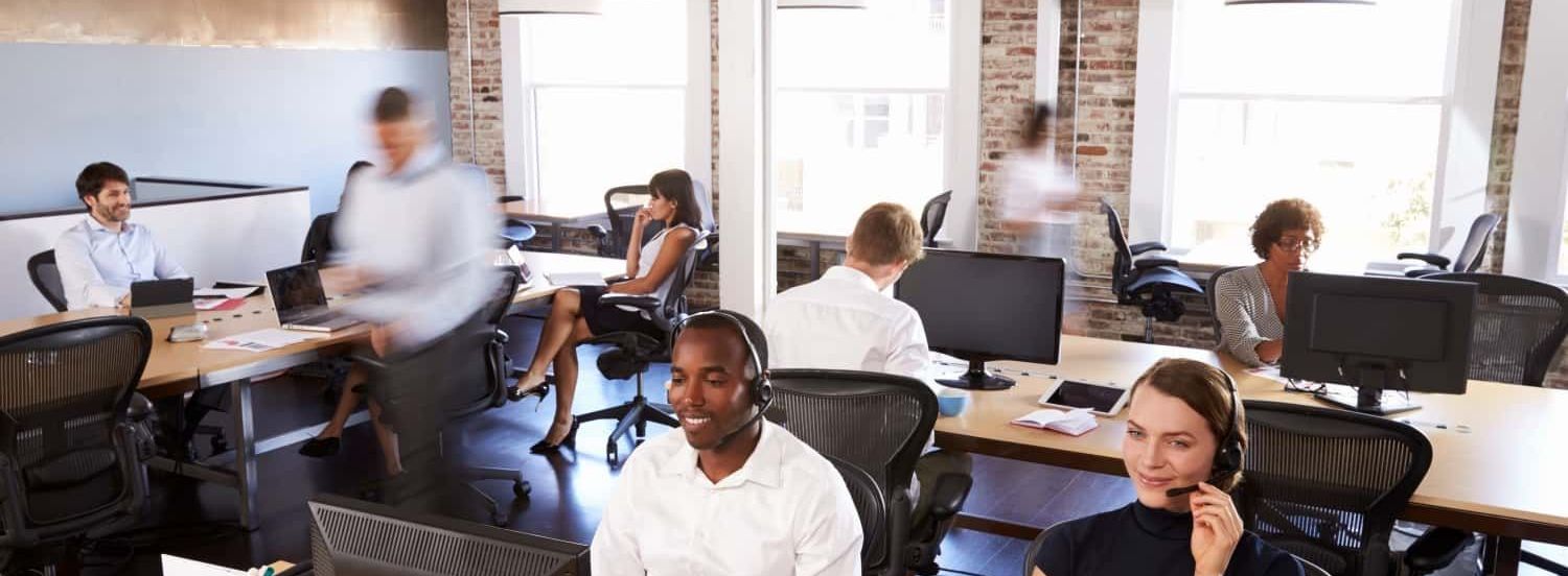 A group of people are sitting at desks in an office wearing headsets.