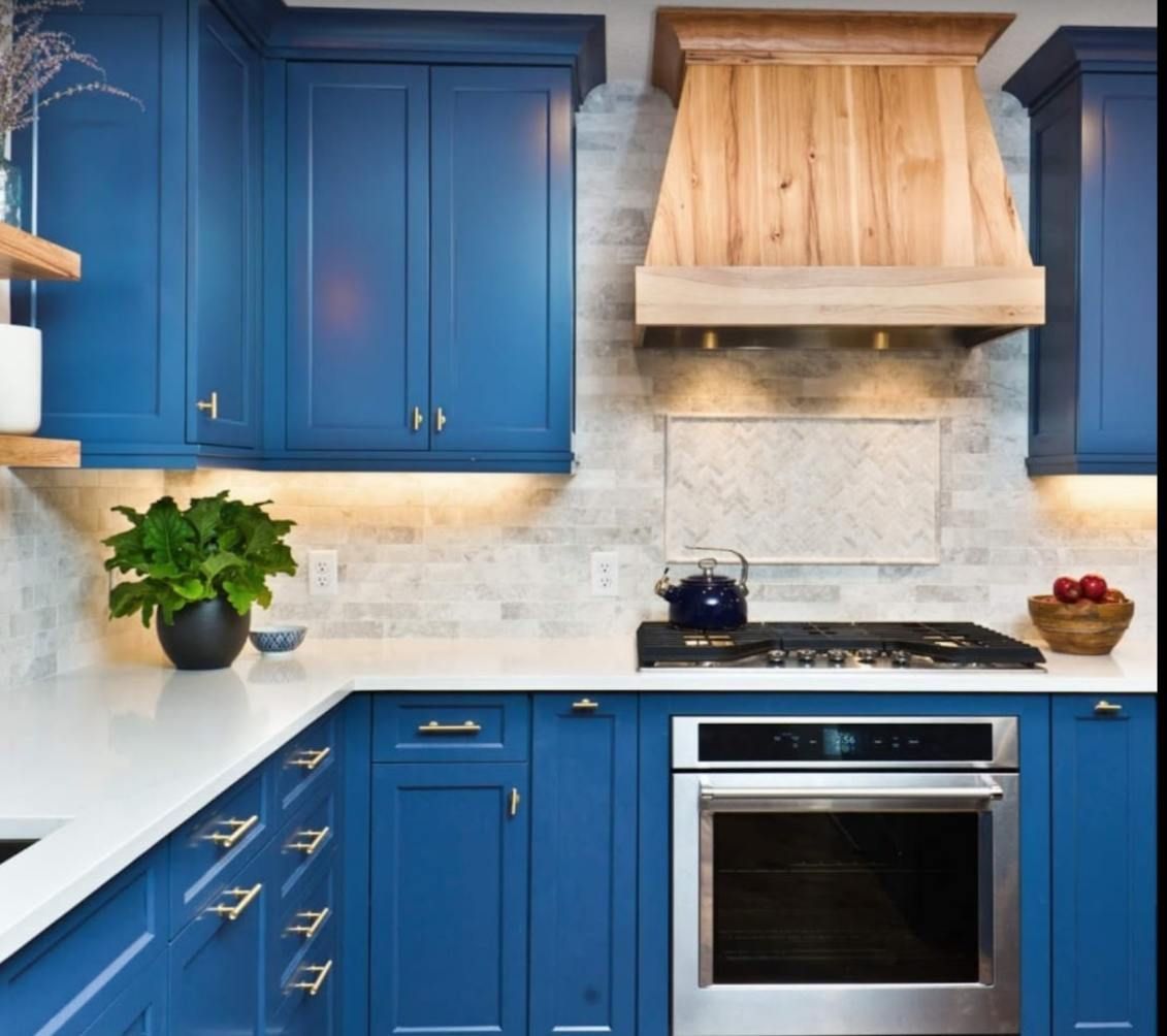 Blue kitchen with white countertops and wooden range hood.