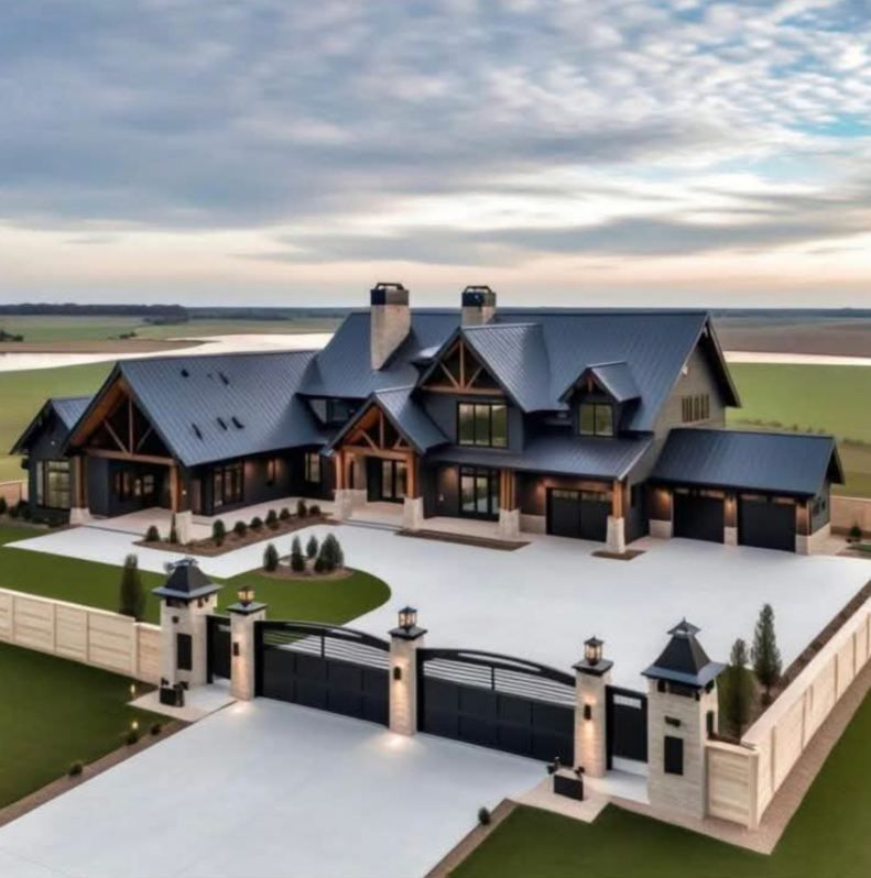 Large, modern house with black roof, wooden accents, and a long driveway with a gated entrance.