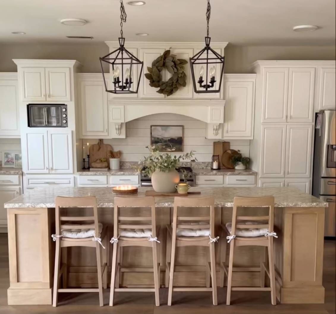 Cozy kitchen with a white island, wooden bar stools, white cabinets, and lantern lights.