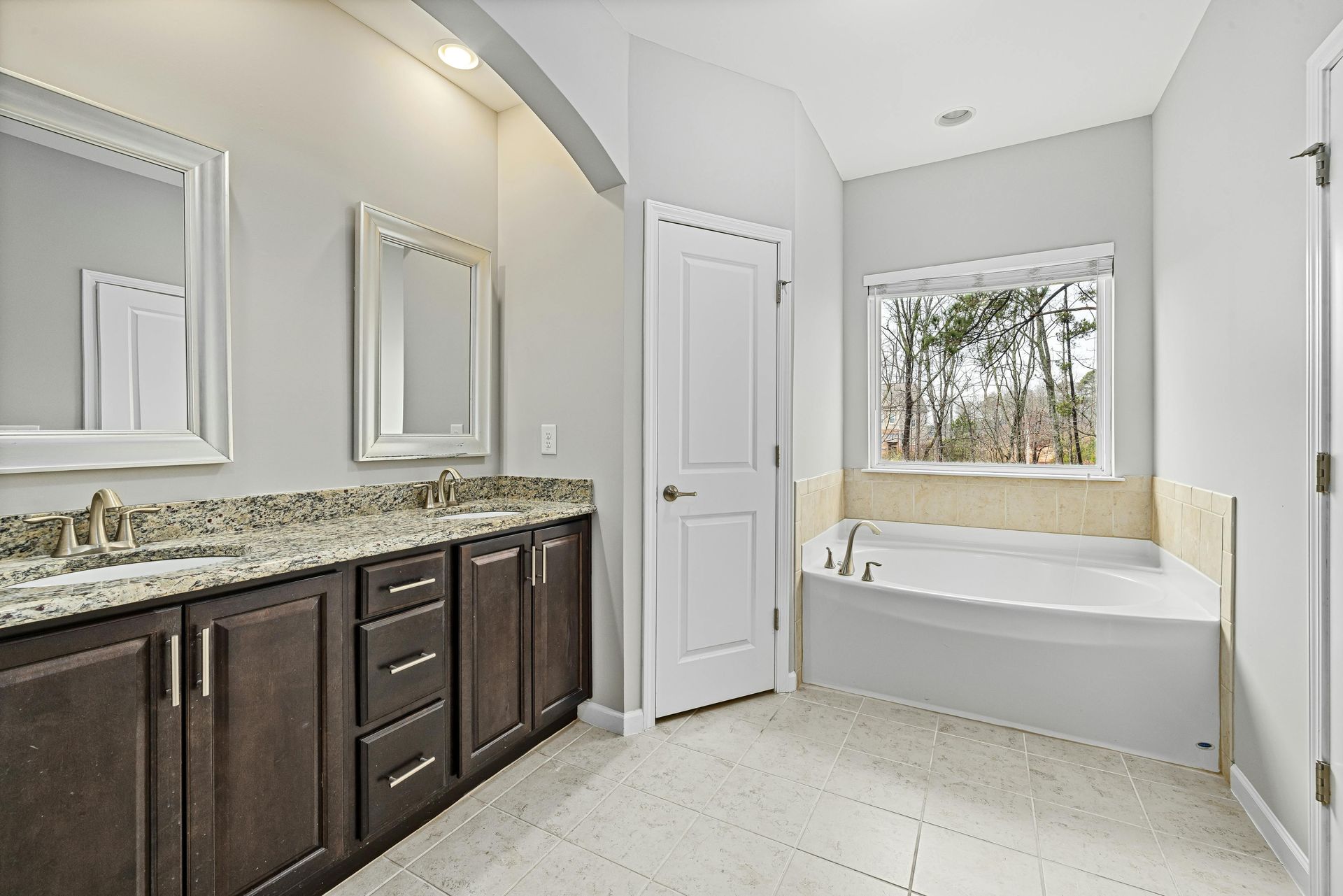 Bathroom with a dark brown vanity, two mirrors, a white door, and a built-in tub with window.