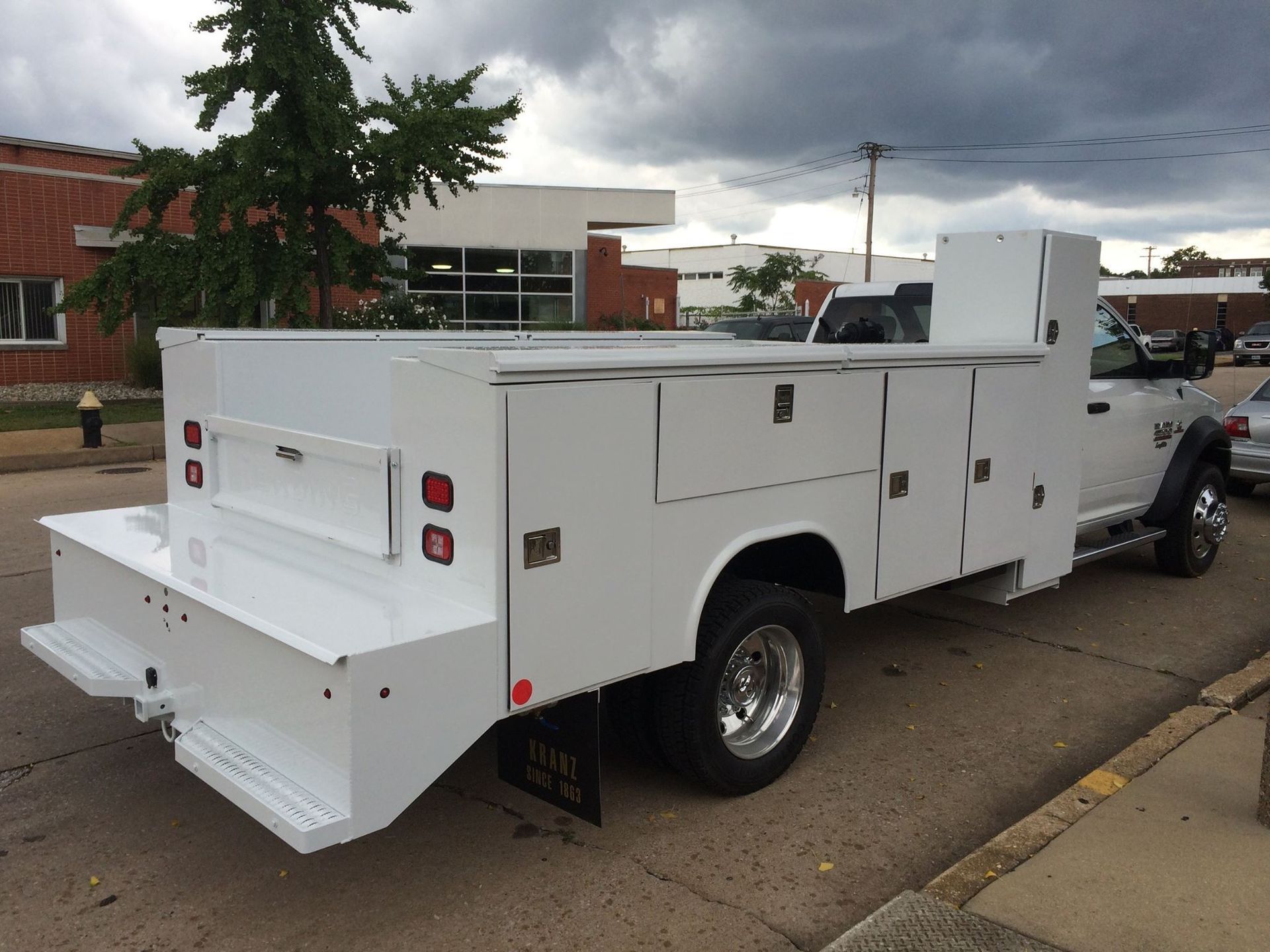 White work truck with a large bed and side compartments parked on a city street.