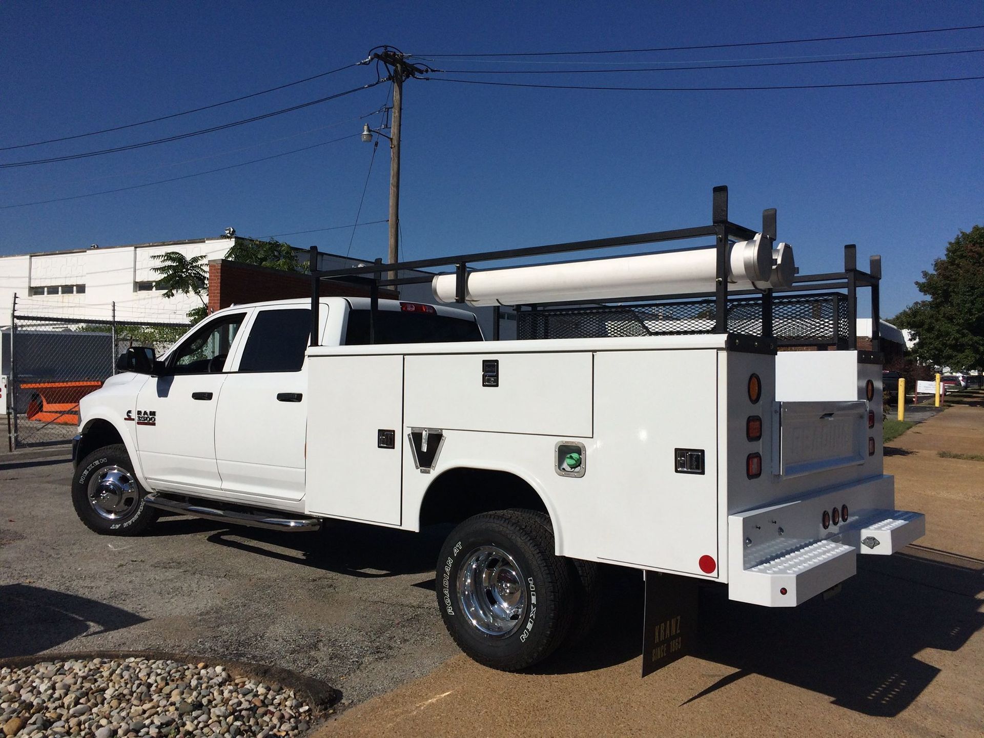 White work truck with storage compartments and ladder rack parked on a street.