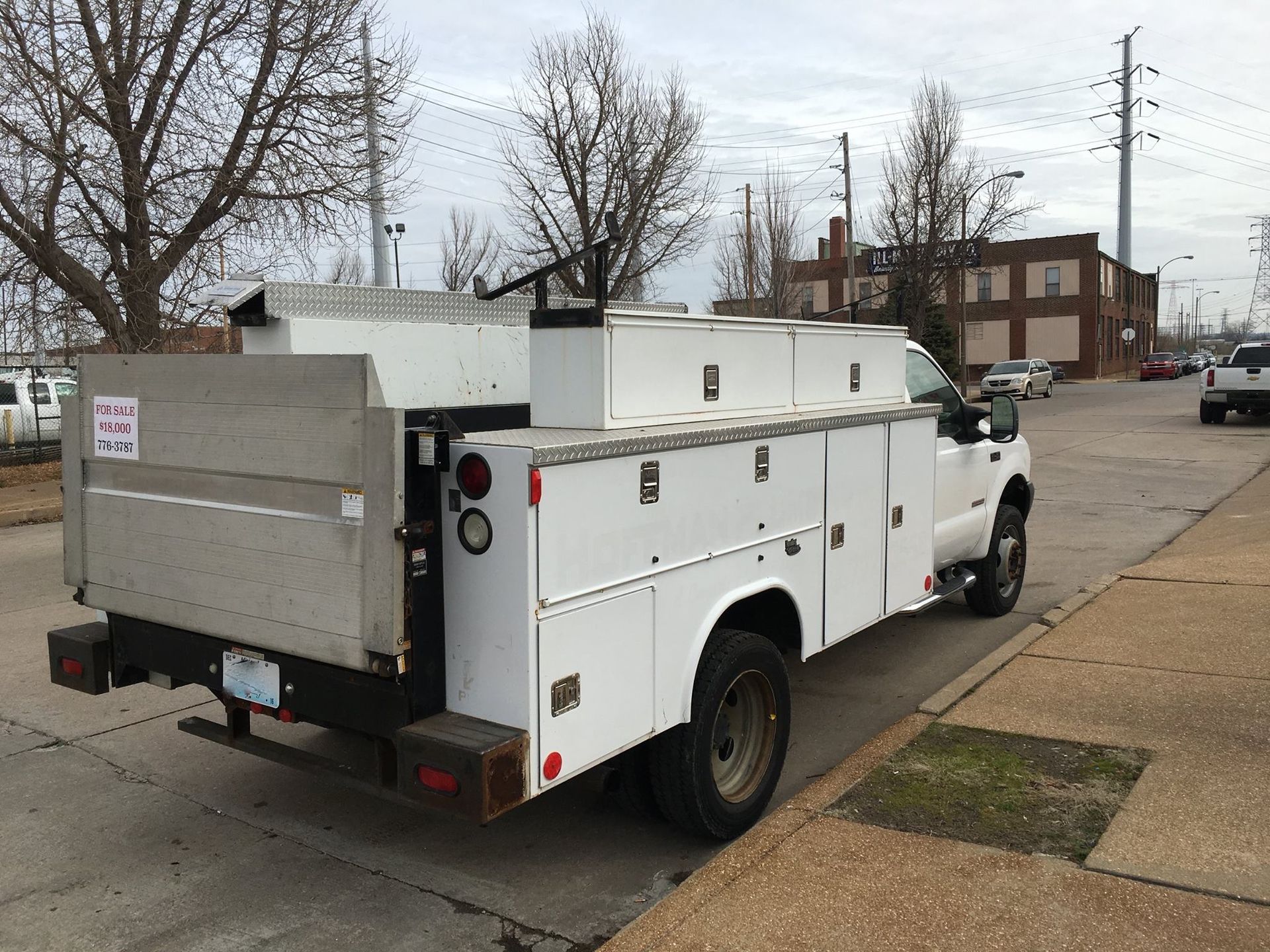 White utility truck parked on a street, against a cloudy sky. A building is in the background.