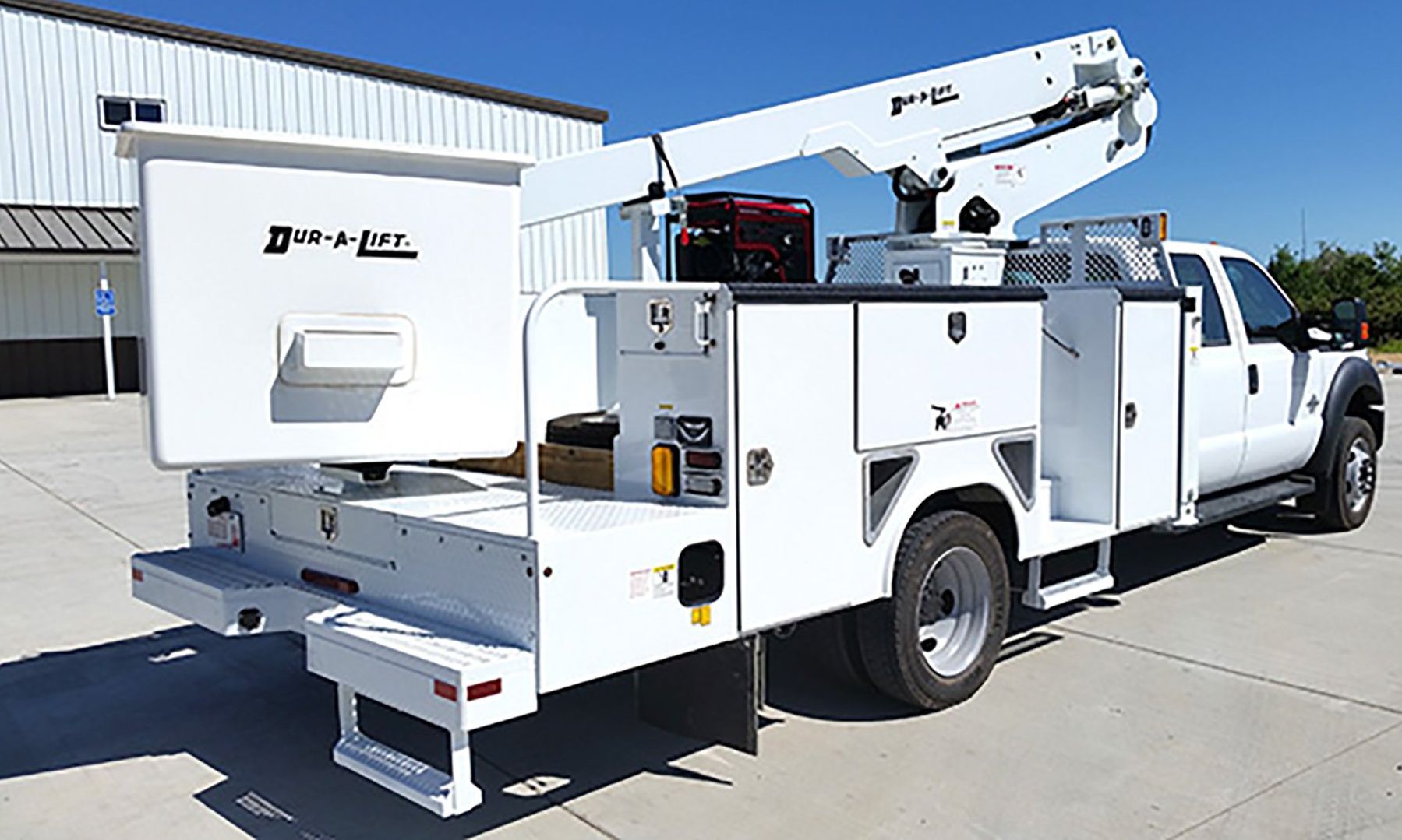 White bucket truck with an elevated boom, parked outdoors on a sunny day.