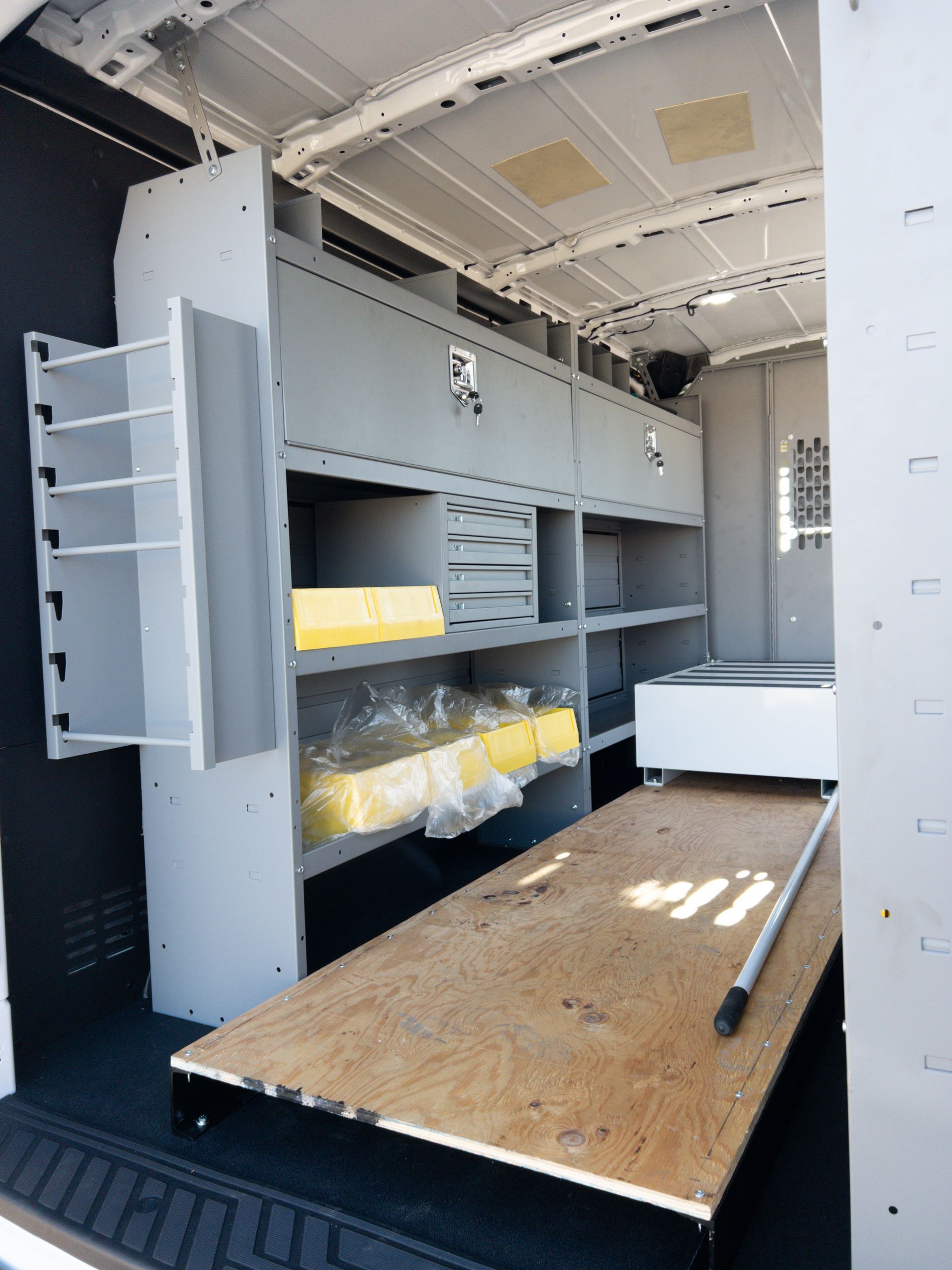 Interior of a work van with gray shelving, wooden platform, and various tools/materials.