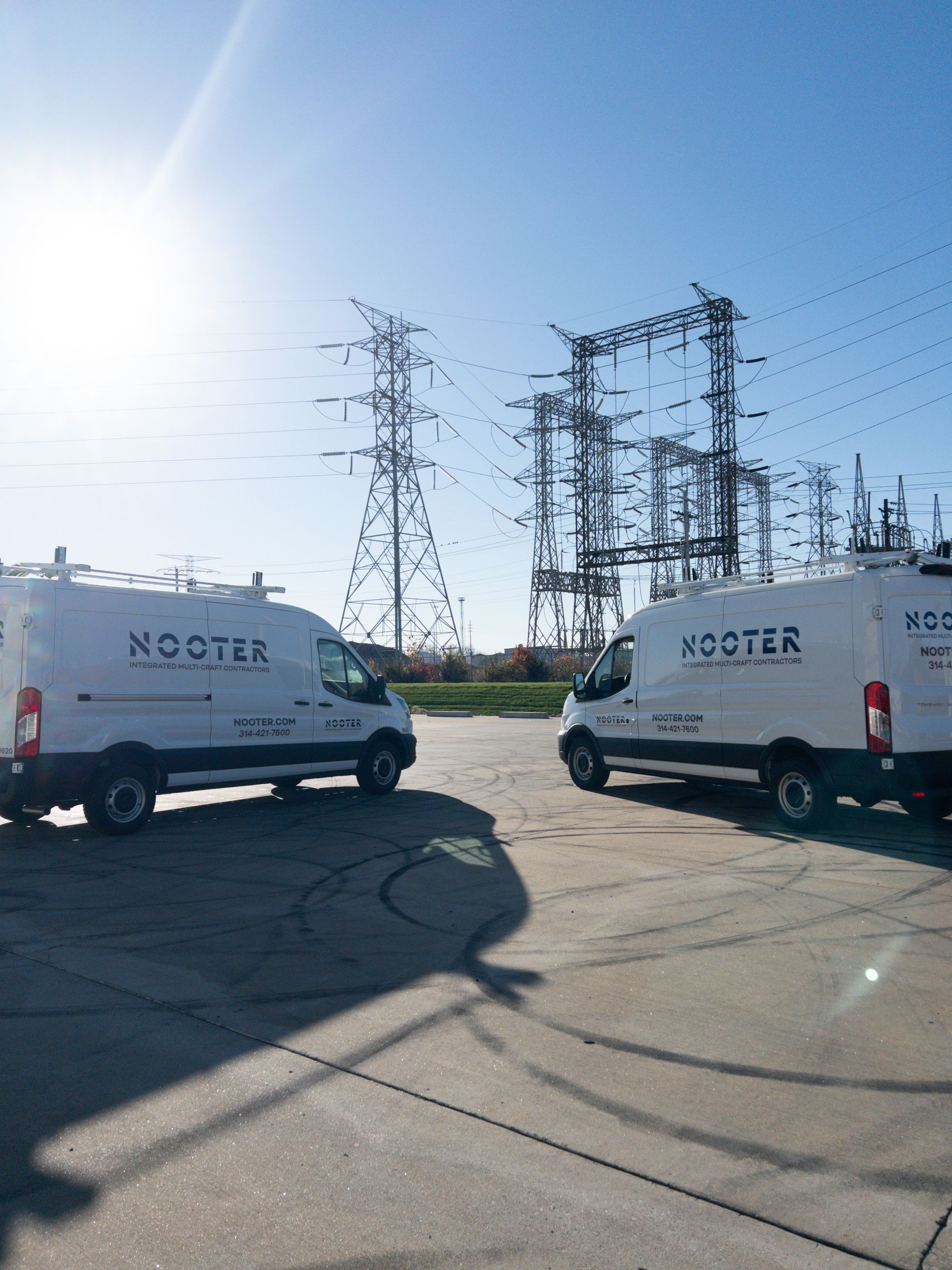 Two white HOOTER vans parked near power lines and a substation on a sunny day.