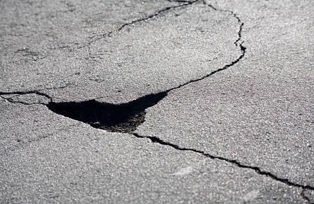 Cracked asphalt with a pothole; gray surface with dark shadows.