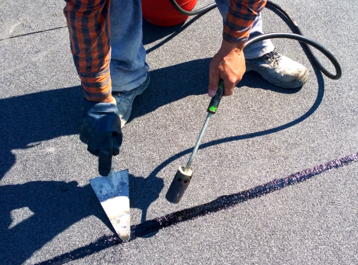 Person using a torch and trowel to seal a seam on a flat roof.